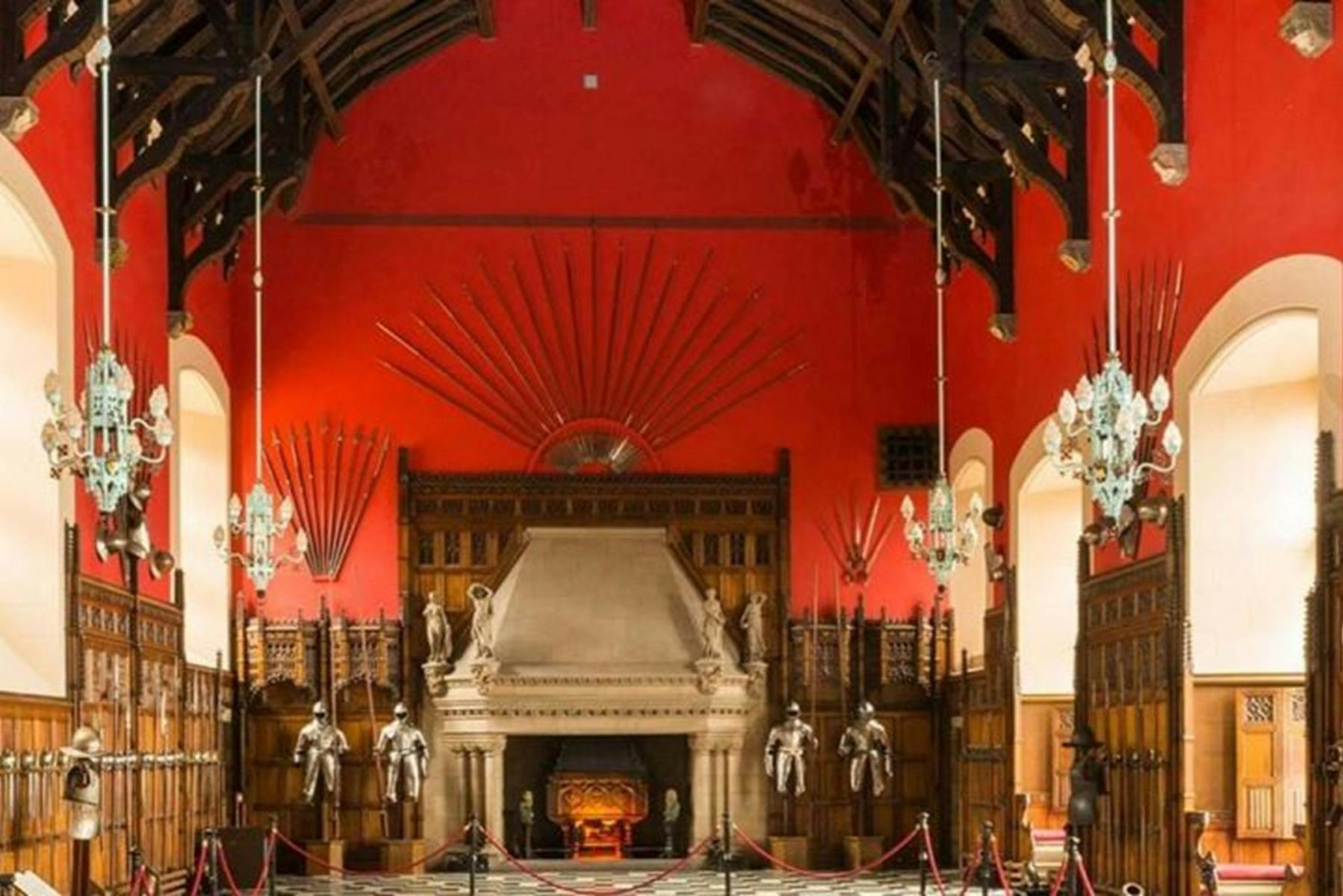 Una grande sala con una parete rossa con un grande camino, spade esposte al muro e armature in mostra.