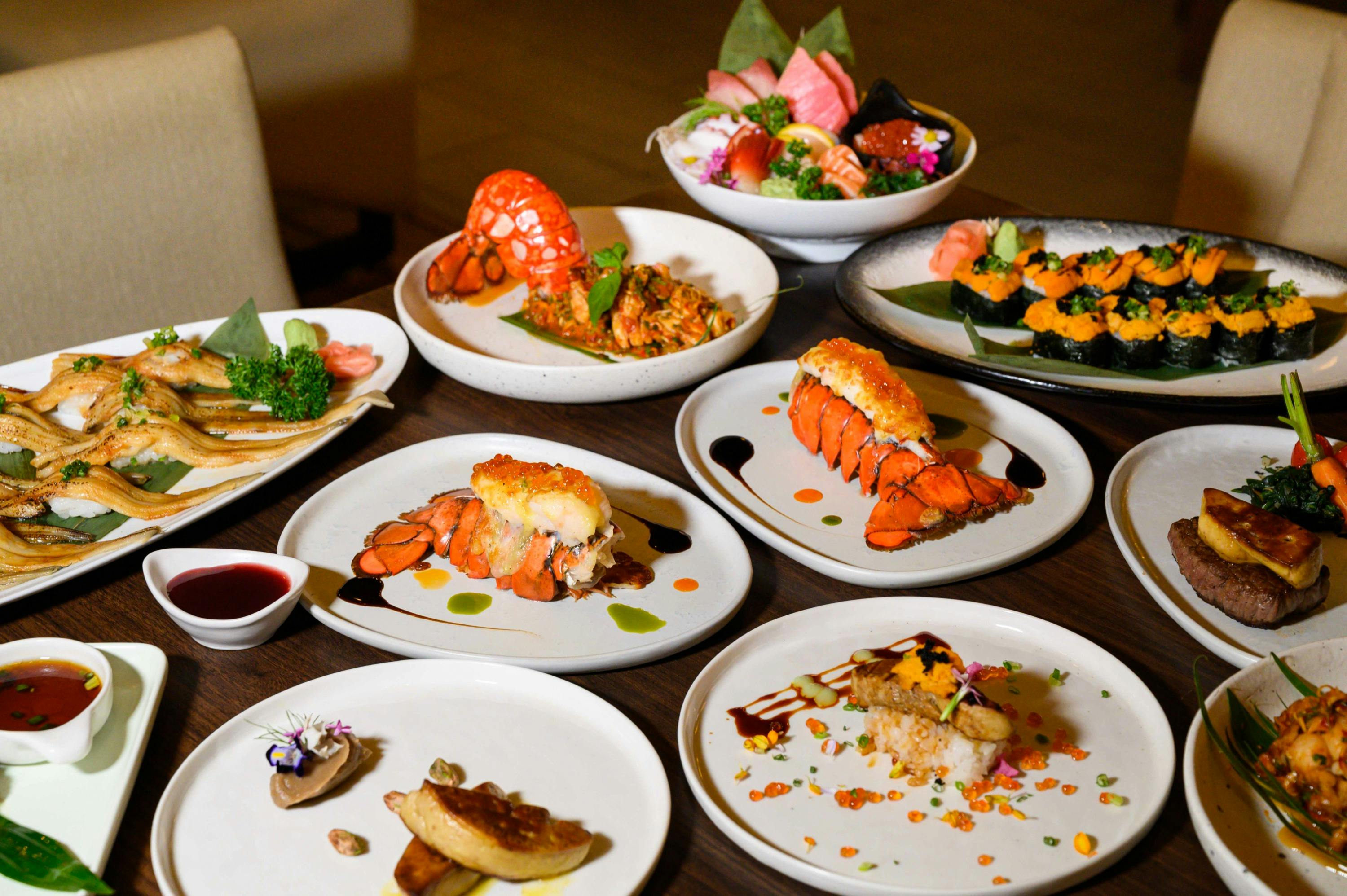An assortment of gourmet dishes on a table, featuring seafood, sushi, and artistic plating with vibrant garnishes.