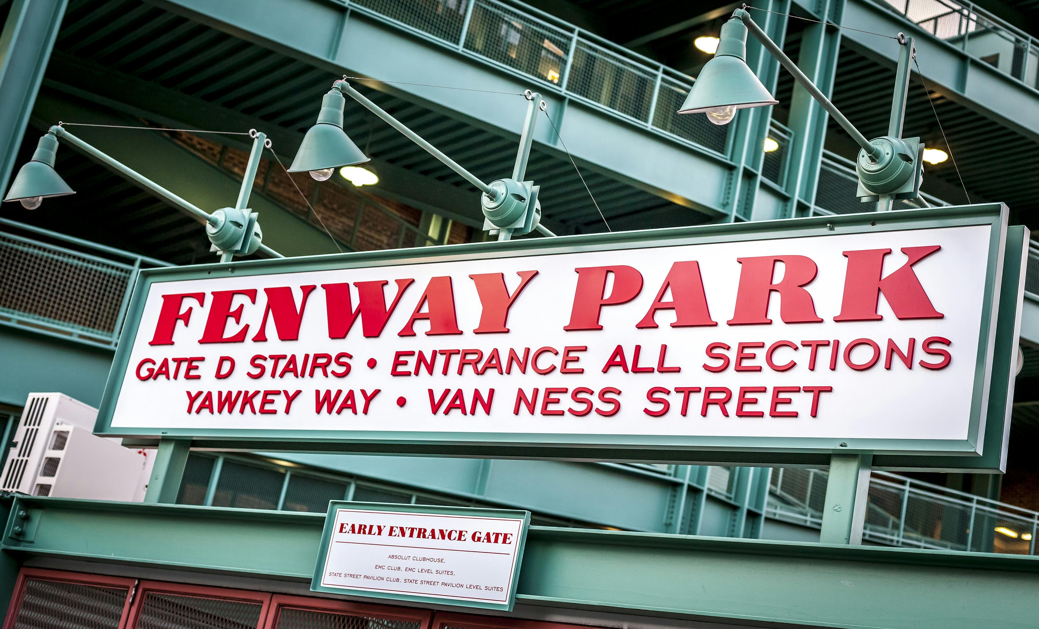 Μια πινακίδα που γράφει &#34;Fenway Park&#34; με οδηγίες προς την Πύλη D, τον Δρόμο Yawkey και την οδό Van Ness, κάτω από πράσινα φώτα και μεταλλικές κατασκευές.