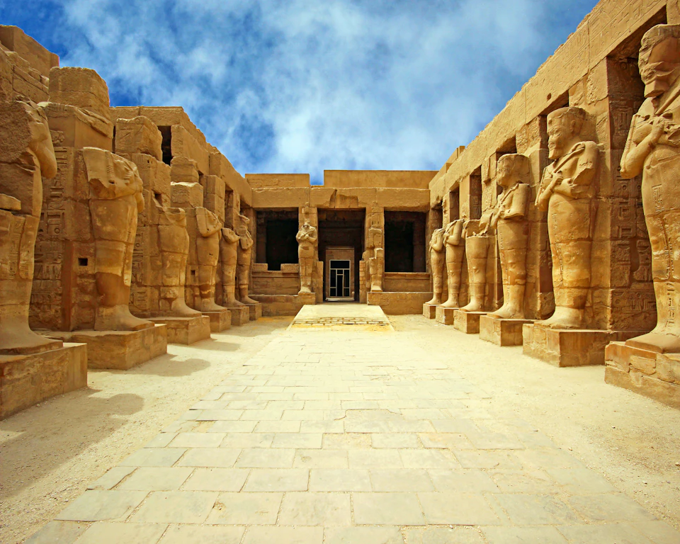 Ancient stone temple entrance with large statues on both sides of a wide, stepped pathway under a blue sky.