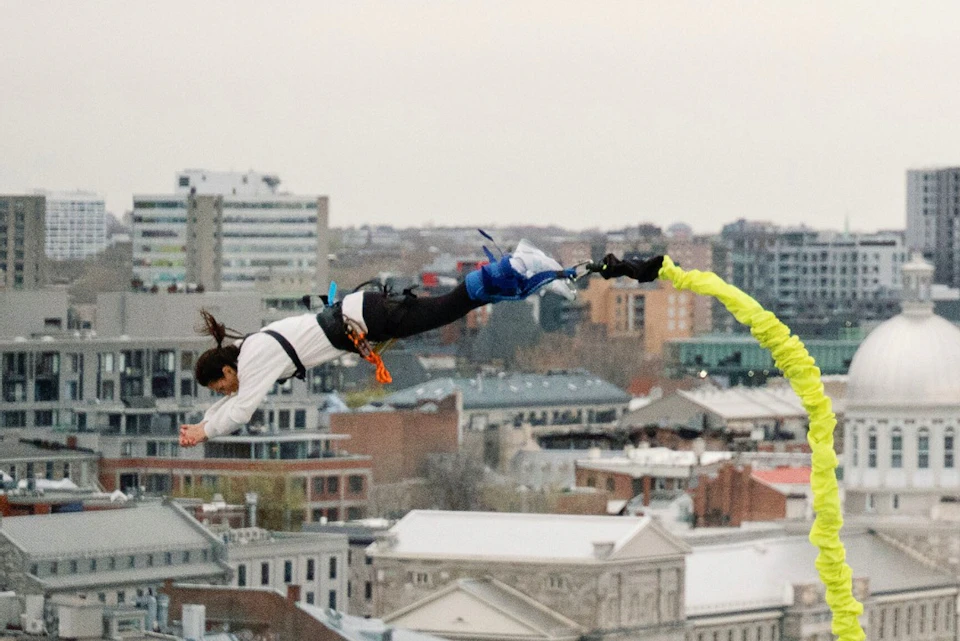 A person in a harness bungee jumping above an urban area with buildings visible in the background.