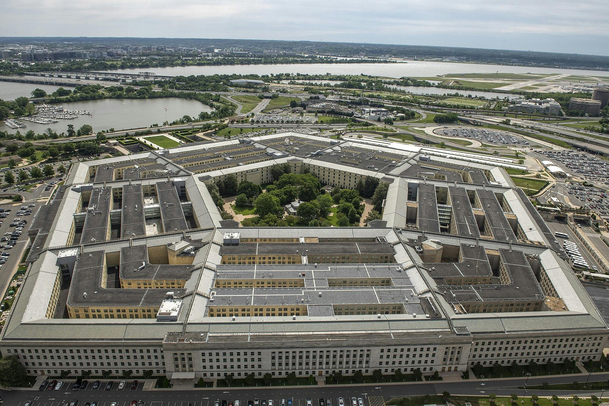 Aerial view of the Pentagon building with its five-sided structure, surrounded by roads, parking lots, water bodies, and greenery.