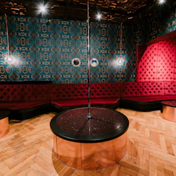 Rum med en central stolpe, omgiven av röda tuftade sittplatser och utsmyckade blå tapeter, med trägolv och dekorativ belysning.