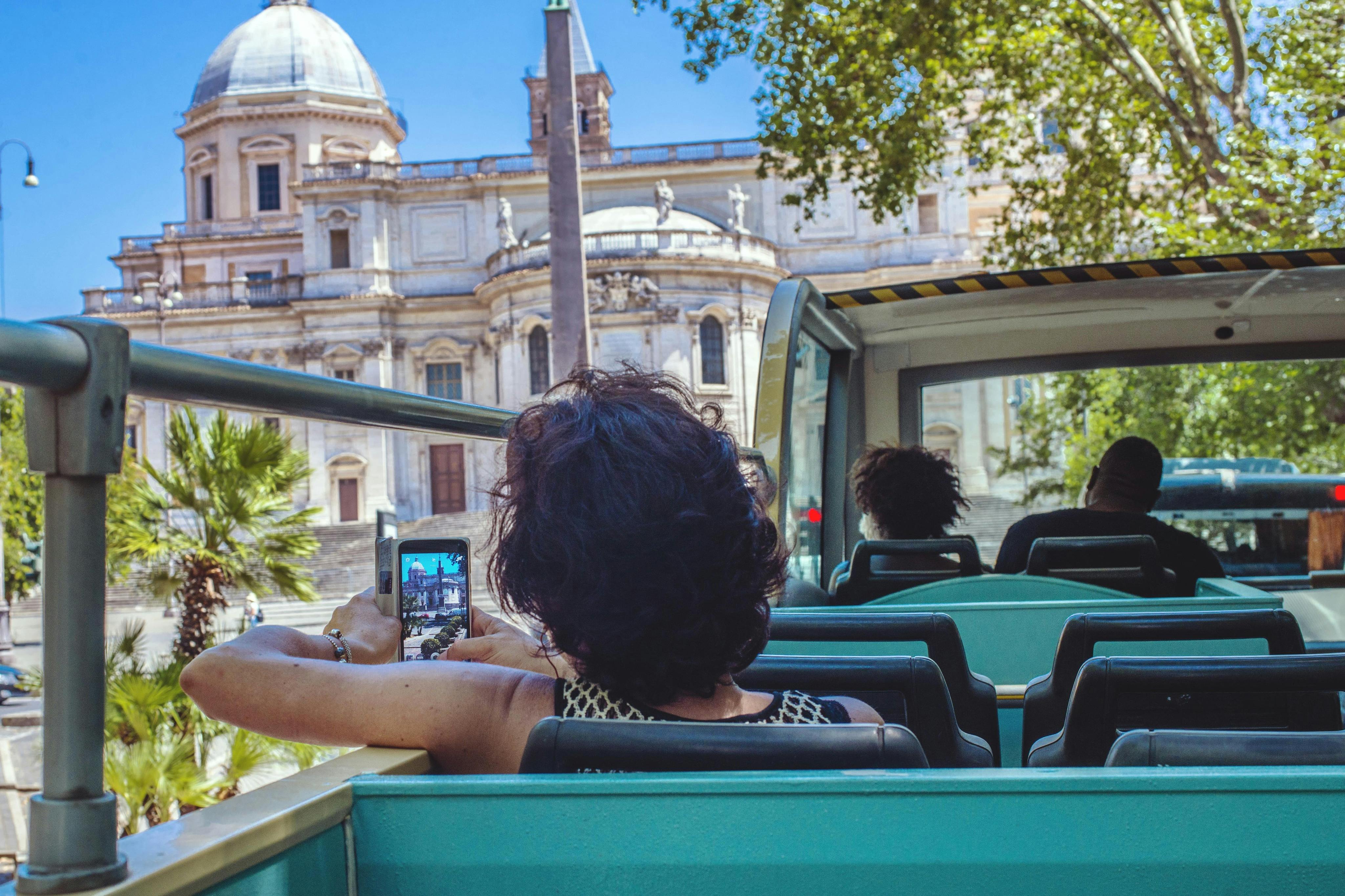 People on an open-top bus with one person taking a photo of an ornate building in the background.