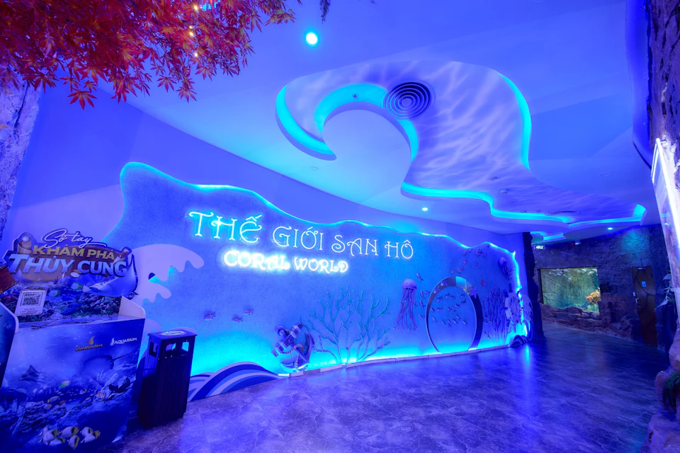 A neon-lit entrance to an attraction named 'Coral World,' featuring aquatic-themed decor and bright blue lighting.