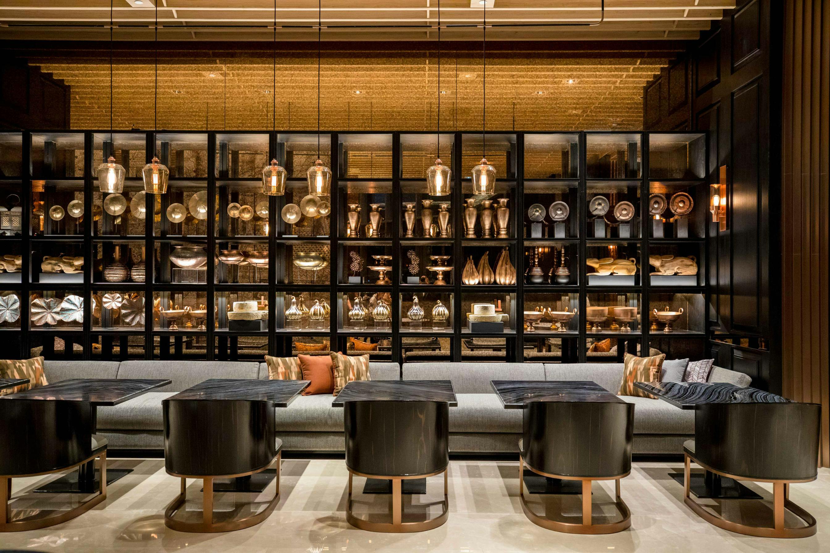 A modern lounge area with black tables and chairs, a gray sofa, and a decorative shelf filled with metallic objects.