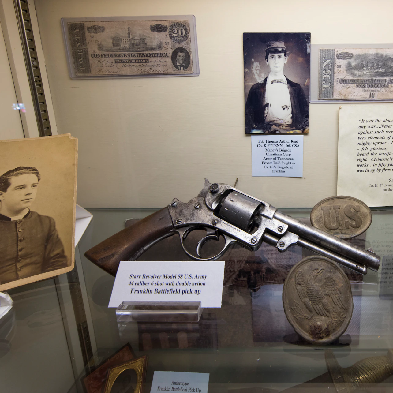 Display case containing a Starr Revolver Model 3, historical photos, currency, and military memorabilia with informational labels.