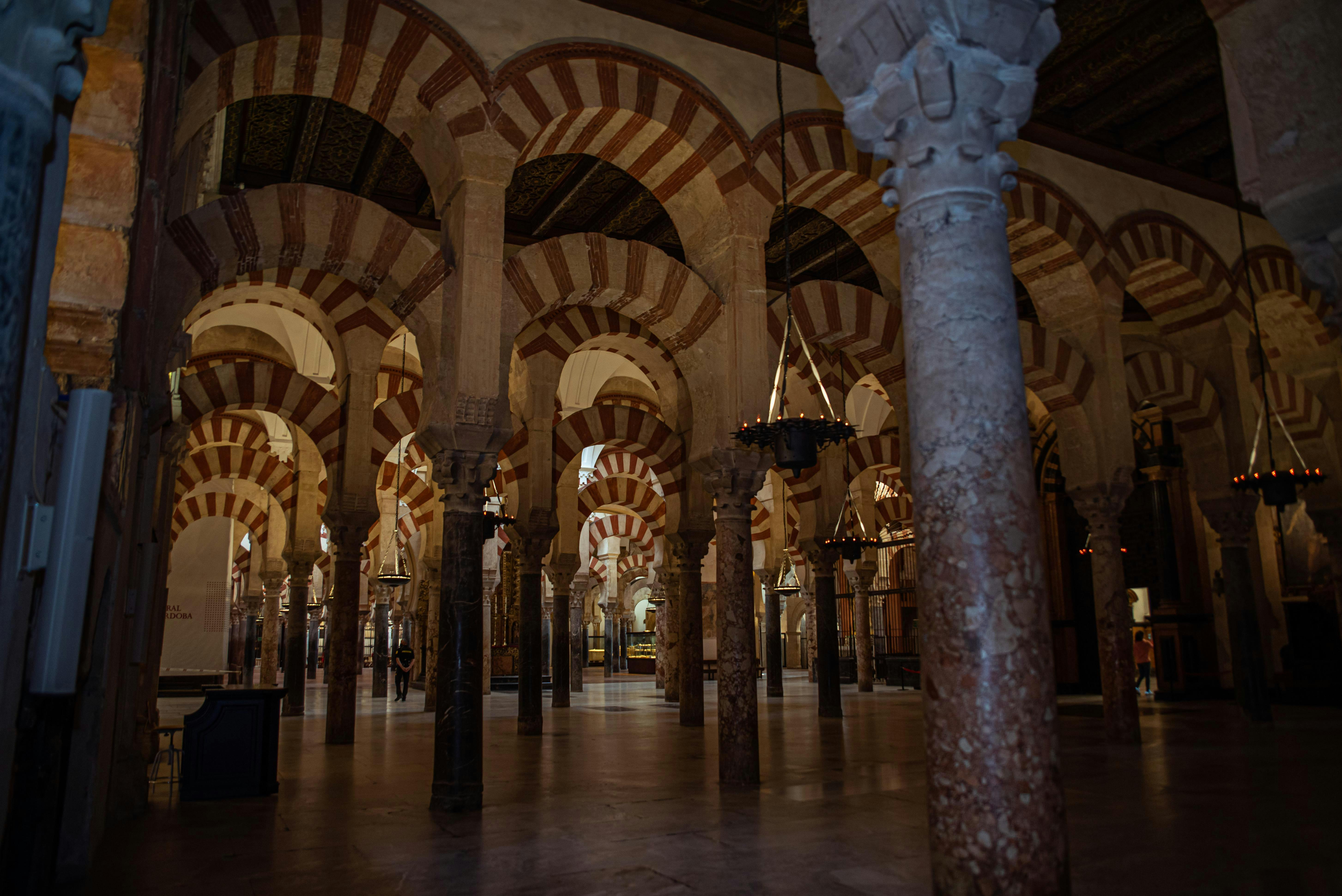 An interior view of a building with numerous striped arches and stone columns. The arches are red and white, creating a distinct pattern.