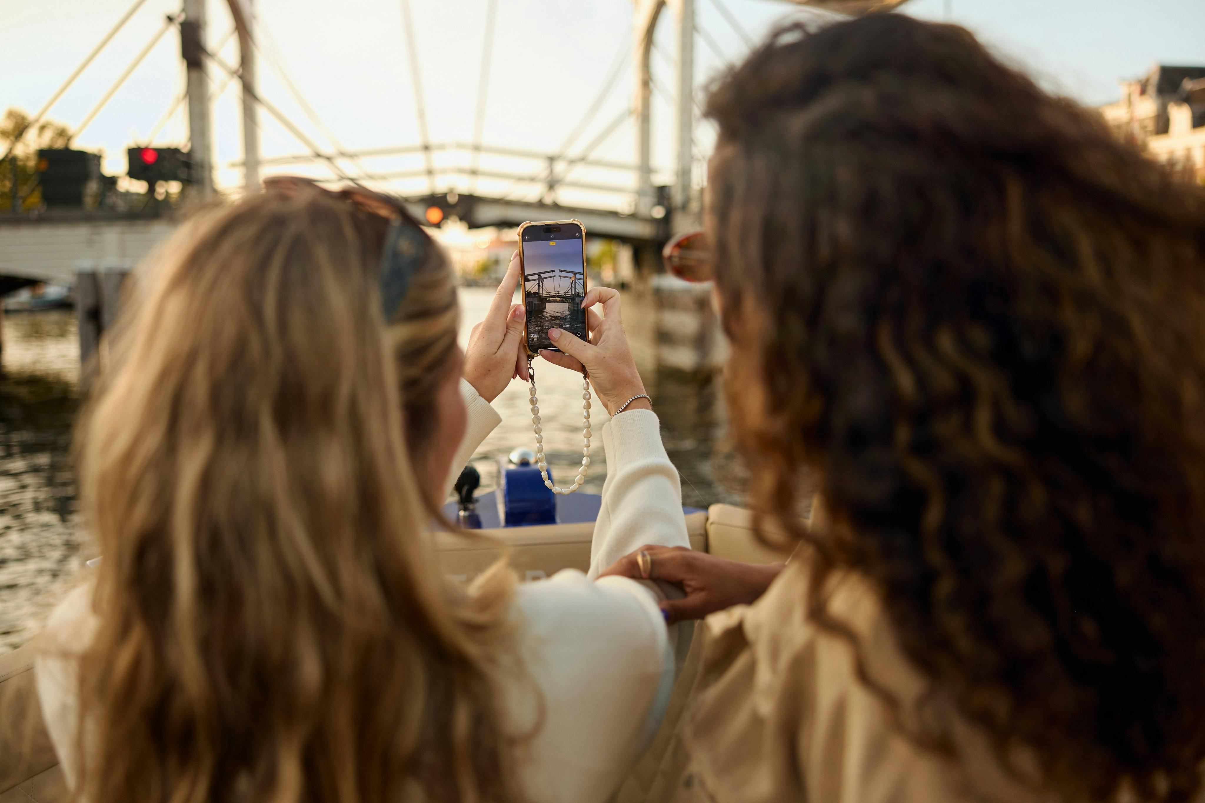 ボートに乗っている2人の人物、1人はスマートフォンで橋の写真を撮っています。