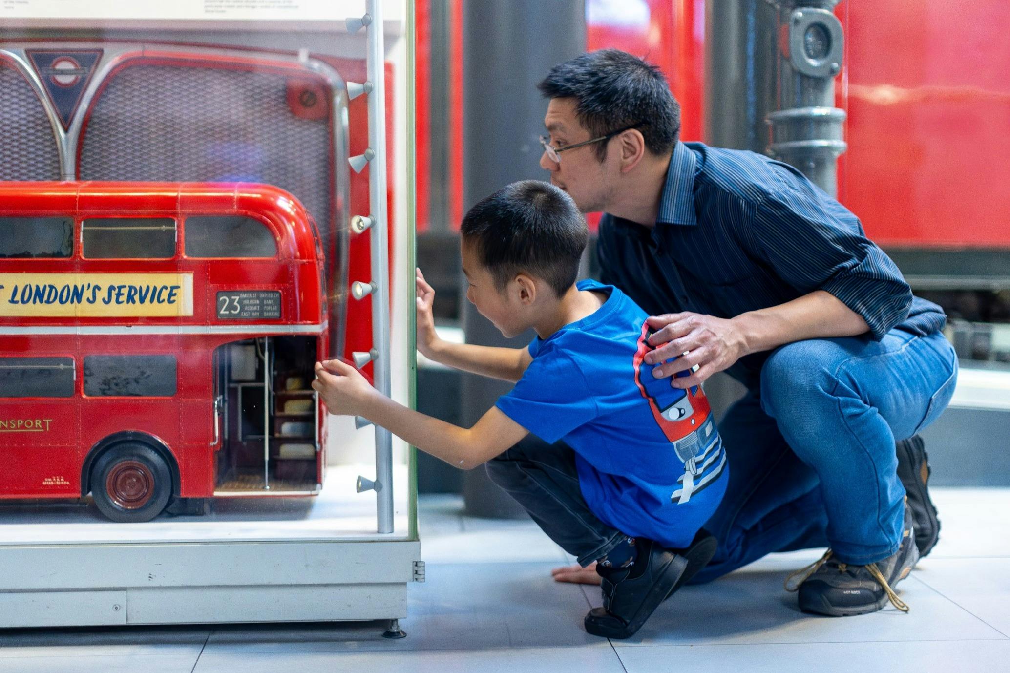 En voksen og et barn undersøger en rød maskine i en museumslignende indstilling, hvor barnet hænger sammen og interagerer med den.