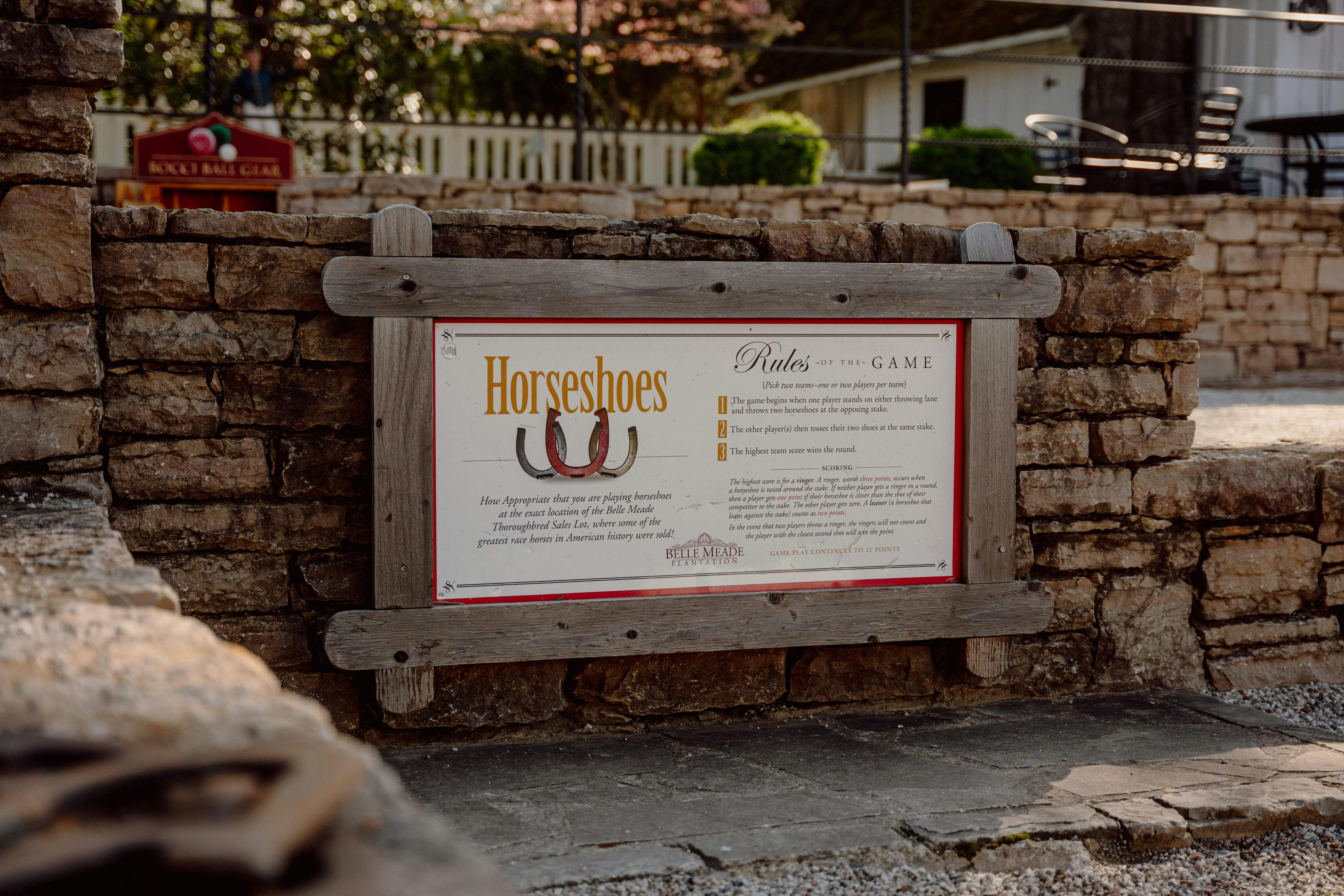 Nápis v dřevěném rámu s nadpisem „Podkovy“ a pravidly hry, umístěný na kamenné zdi ve venkovním prostředí.