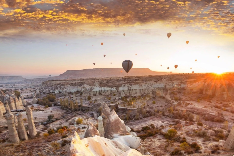 Hot air balloons floating over a rocky landscape at sunset, with a sky filled with scattered clouds.