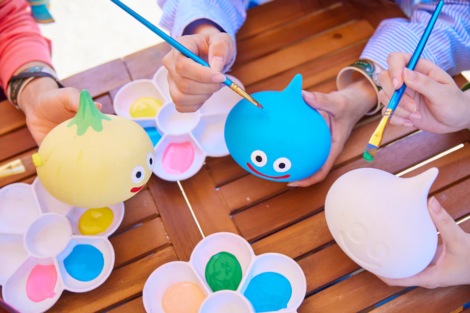 People painting colorful, cartoon-faced figurines at a table with paint palettes and brushes.