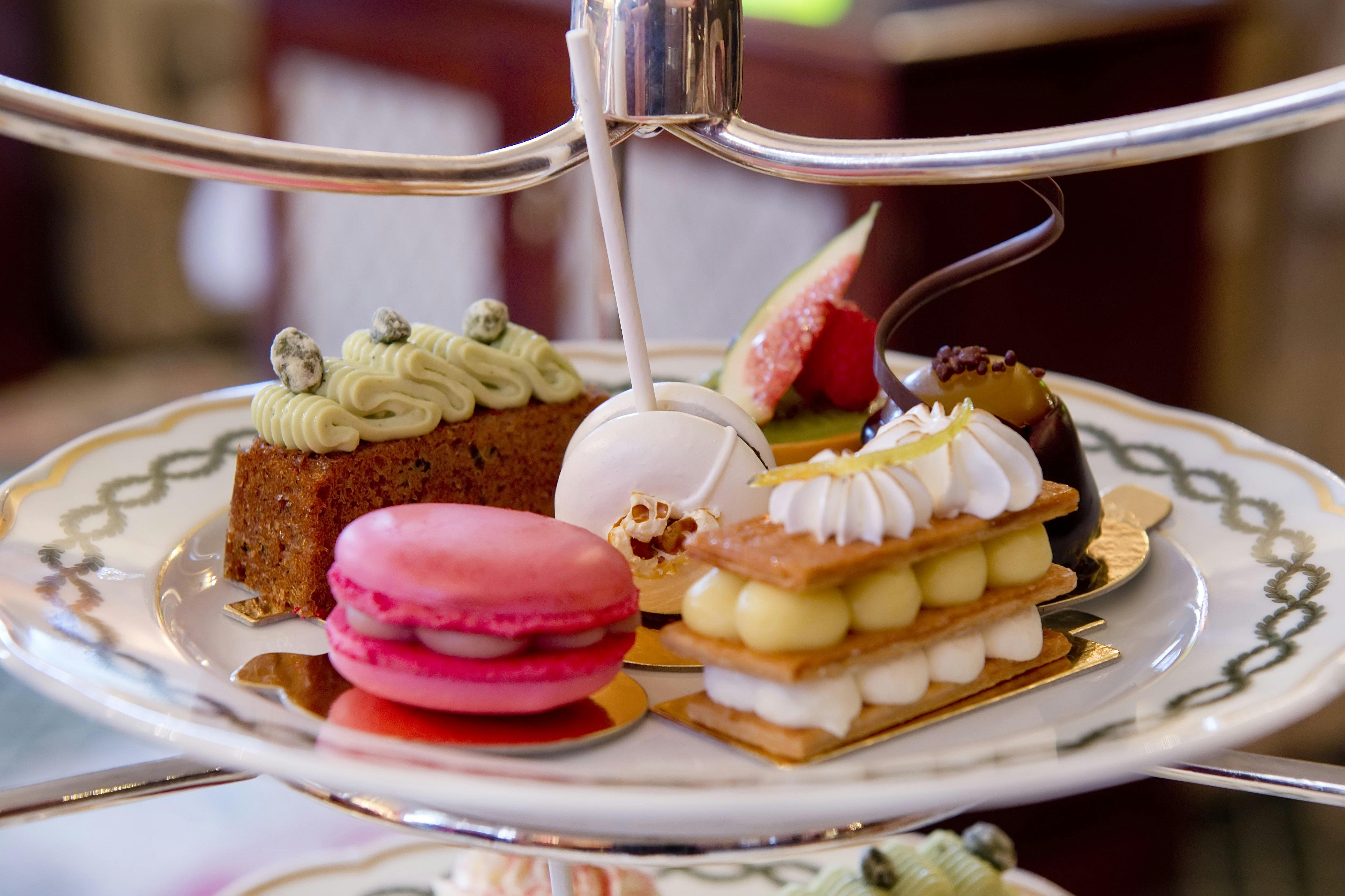 An assortment of colorful pastries on a tiered tray, including a macaron, lollipop, cake, and fruit tart.