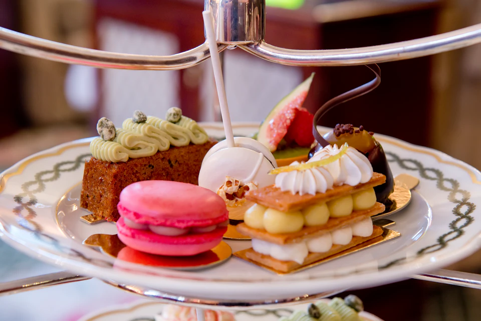 An assortment of colorful pastries on a tiered tray, including a macaron, lollipop, cake, and fruit tart.