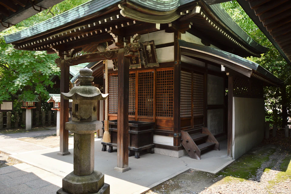 A traditional Japanese wooden shrine with a stone lantern in the foreground, surrounded by trees.