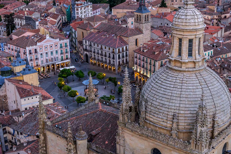 Aerial view of a historic town square surrounded by old buildings with a church dome and bell tower in the foreground.