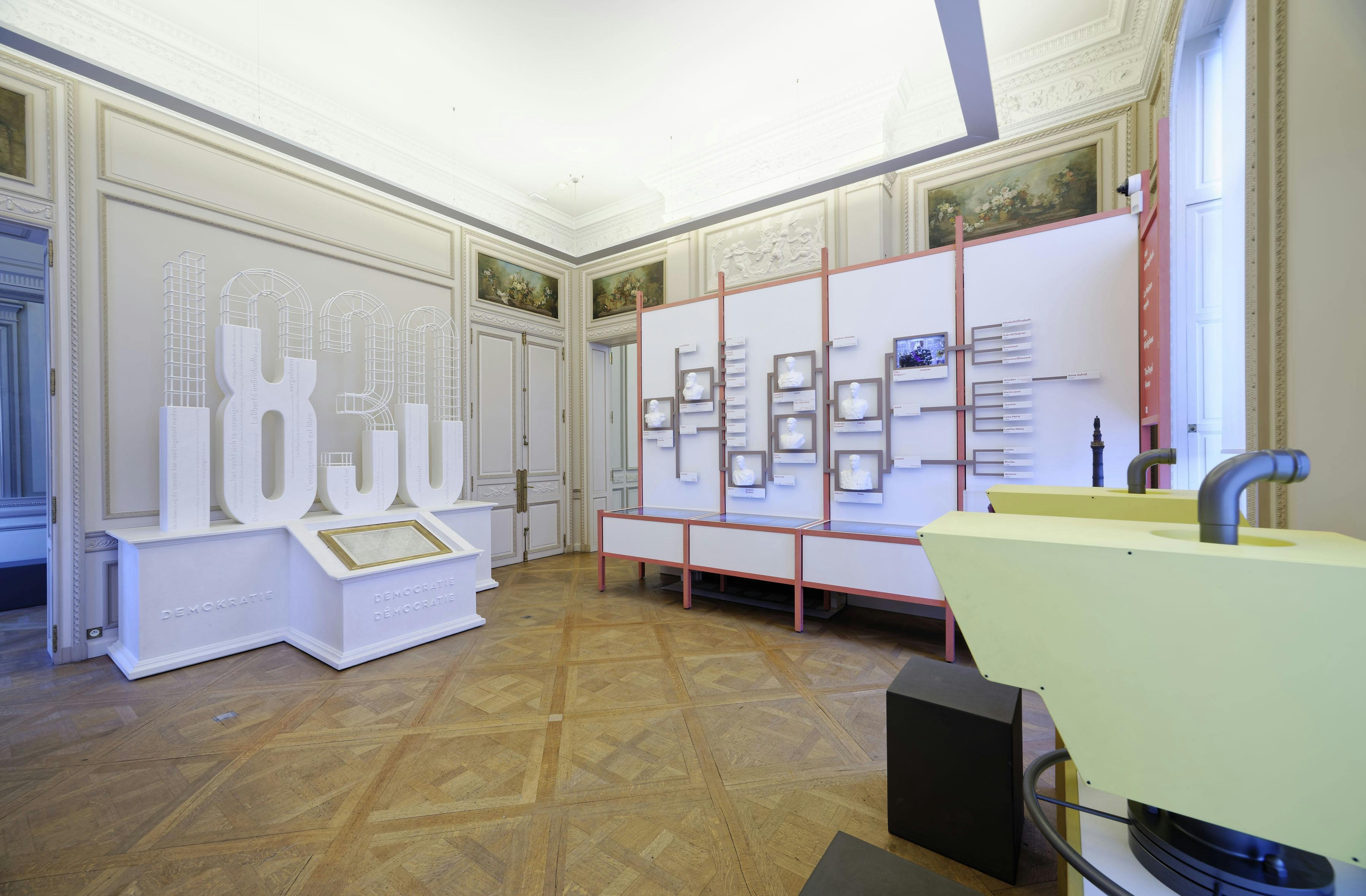 Una moderna sala d&#39;exposicions amb estructures de color blanc i rosa, art mural emmarcat i un pòdium amb pantalla tàctil sobre terra de fusta.