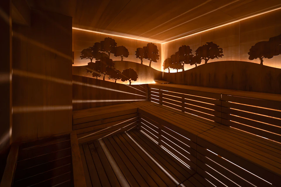 A wooden sauna interior with bench seating and illuminated wall art depicting trees, creating a relaxing ambiance.