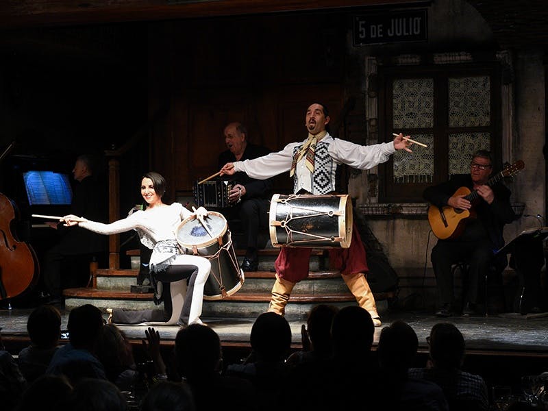 무대 위의 연주자: 드럼을 연주하는 남녀, 아코디언을 연주하는 또 다른 남자, 기타를 연주하는 네 번째 남자.