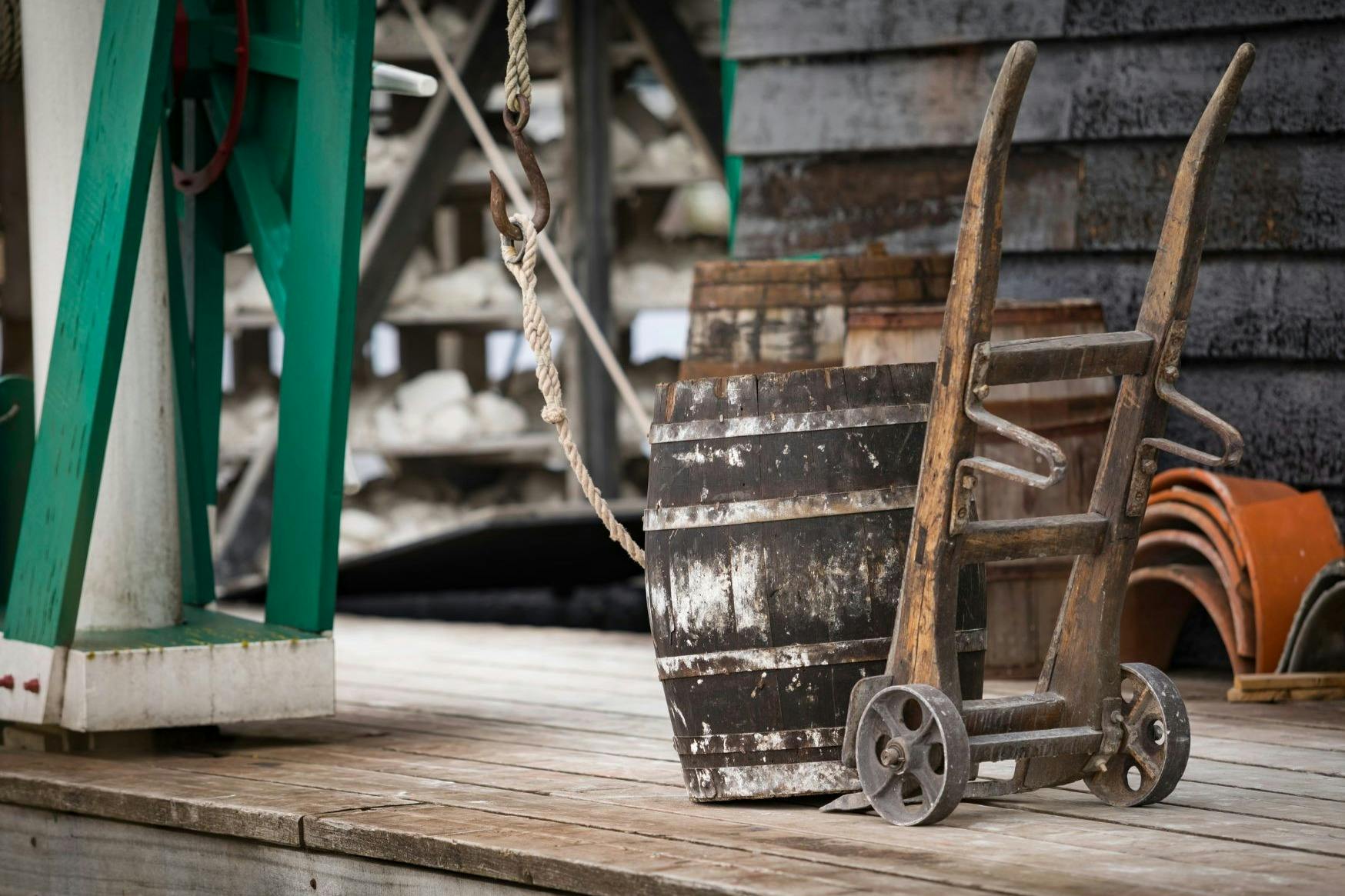 風化した木製の樽が台車の上に置かれた木製のデッキには、ロープと緑色の金属構造が付いています。