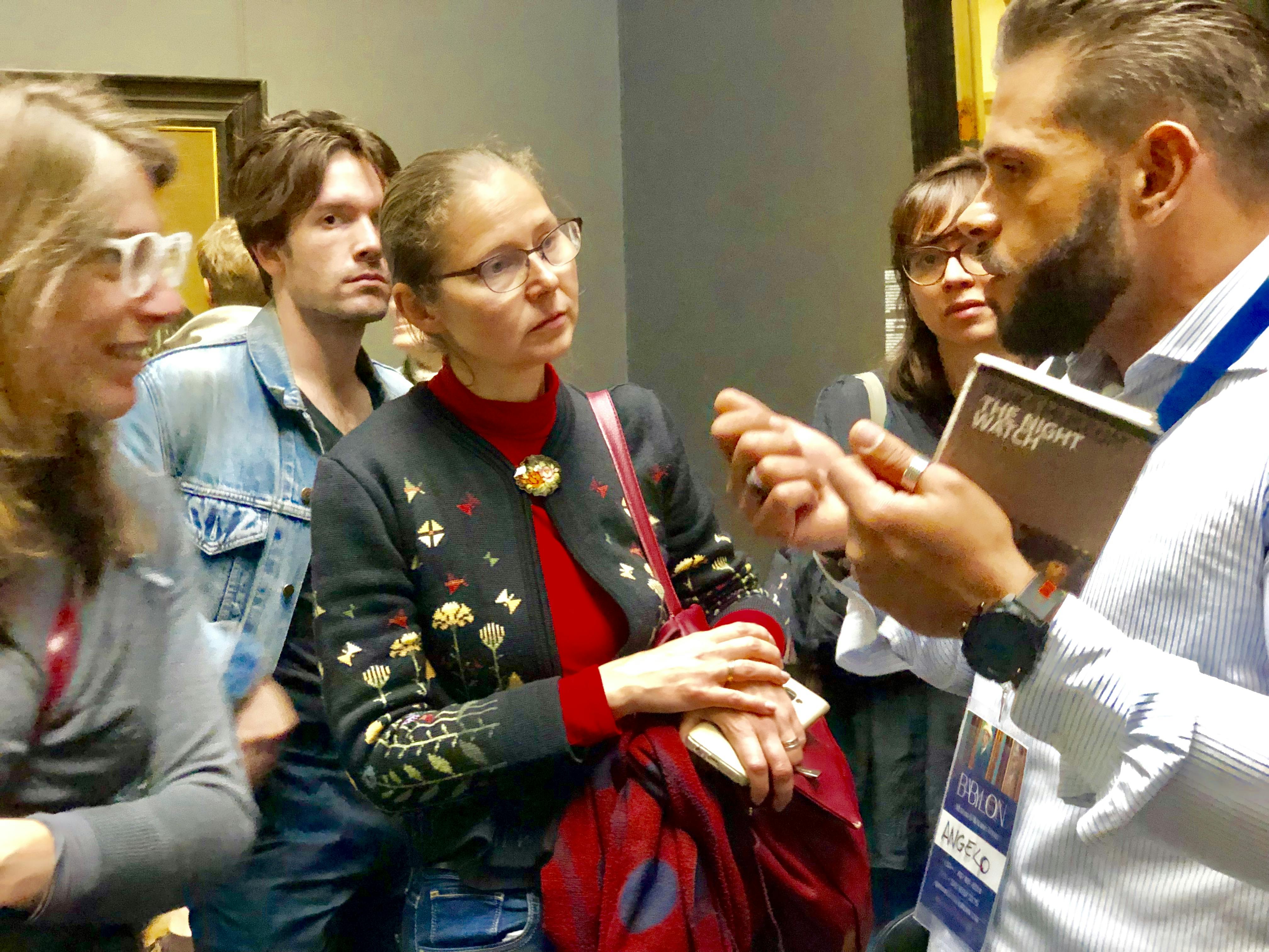 一群人，包括一个戴着花卉毛衣的眼镜的女人，专注地听着别人用手做手势。