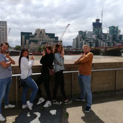 Fem personer poserar lekfullt framför en flod, med stadsbyggnader och byggkranar i bakgrunden.