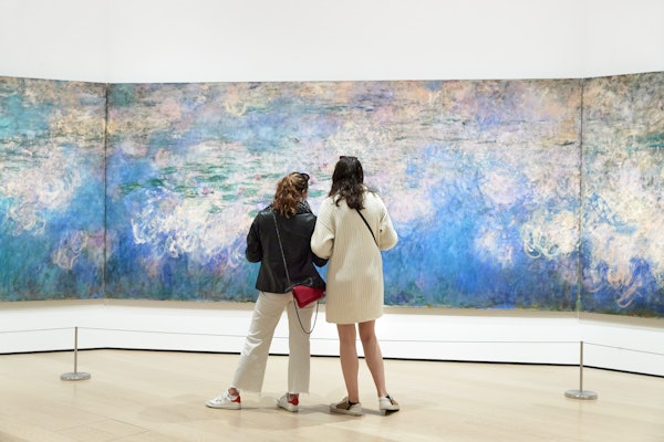To kvinder står foran et stort, farverigt abstrakt maleri i et kunstgalleri og ser på og diskuterer det.