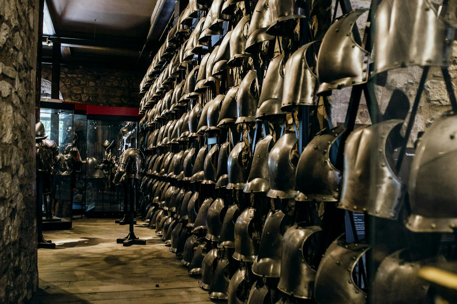 Rows of metal helmets and armor displayed on stands in a dimly lit room, with a glass display case in the background.