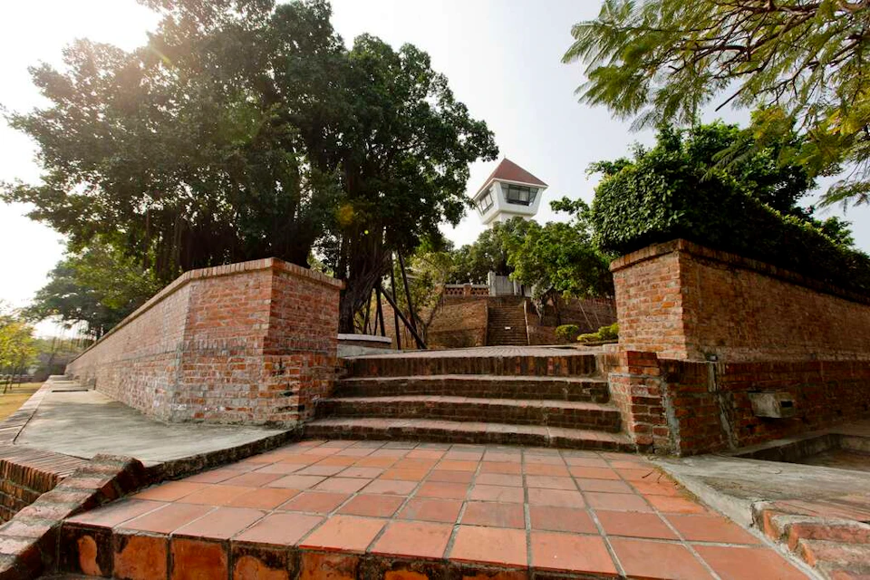 Brick stairs leading to a tower with a red roof, surrounded by trees and greenery under a sunny sky.