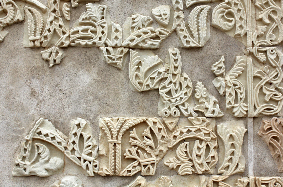 A close-up of a stone wall featuring intricate, partially broken carvings with leaf and geometric patterns.