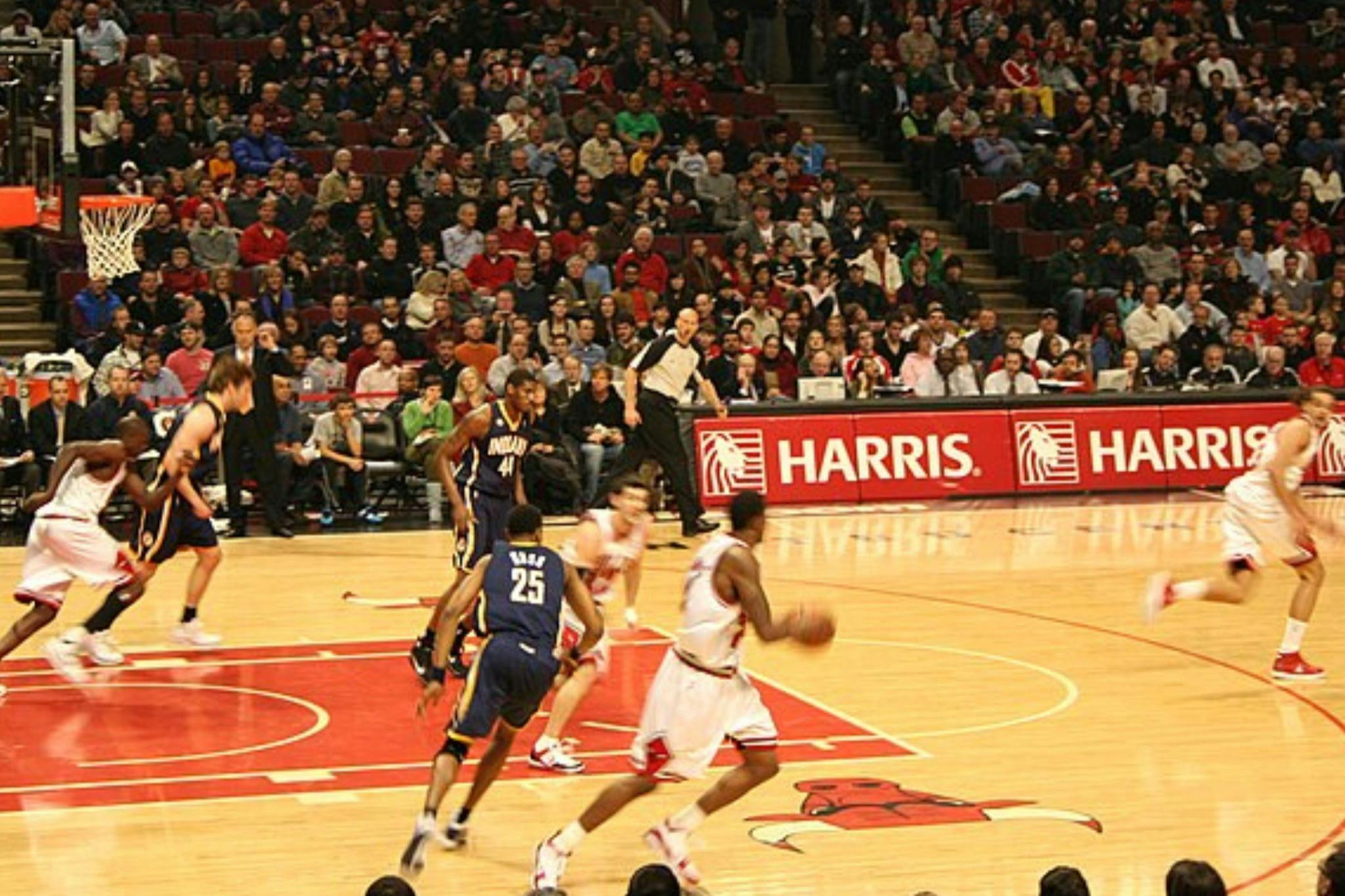 Basketball players in action on a court during a game with a crowd of spectators in the background.