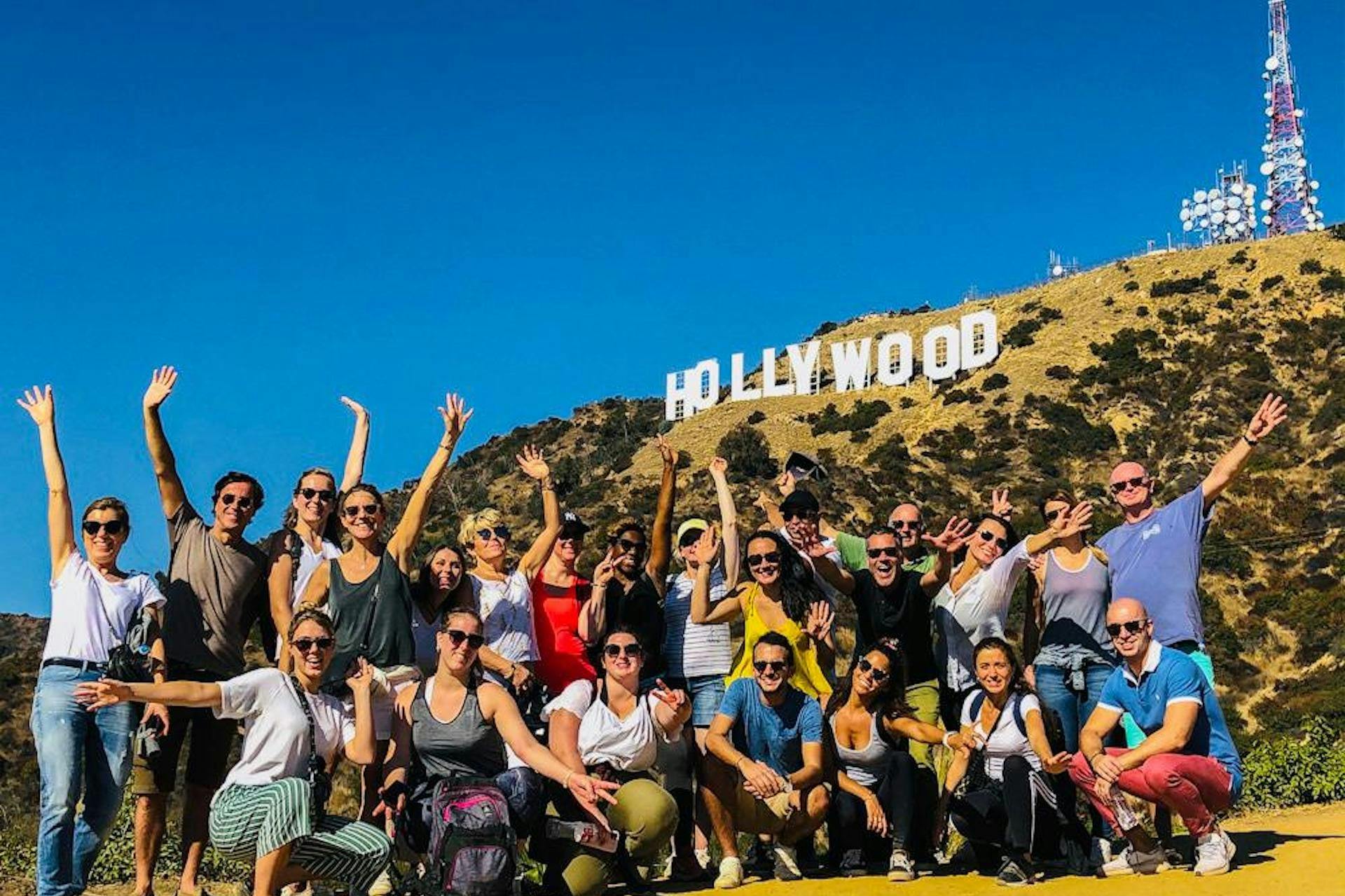 A group of people posing in front of the Hollywood sign on a sunny day with a clear blue sky.