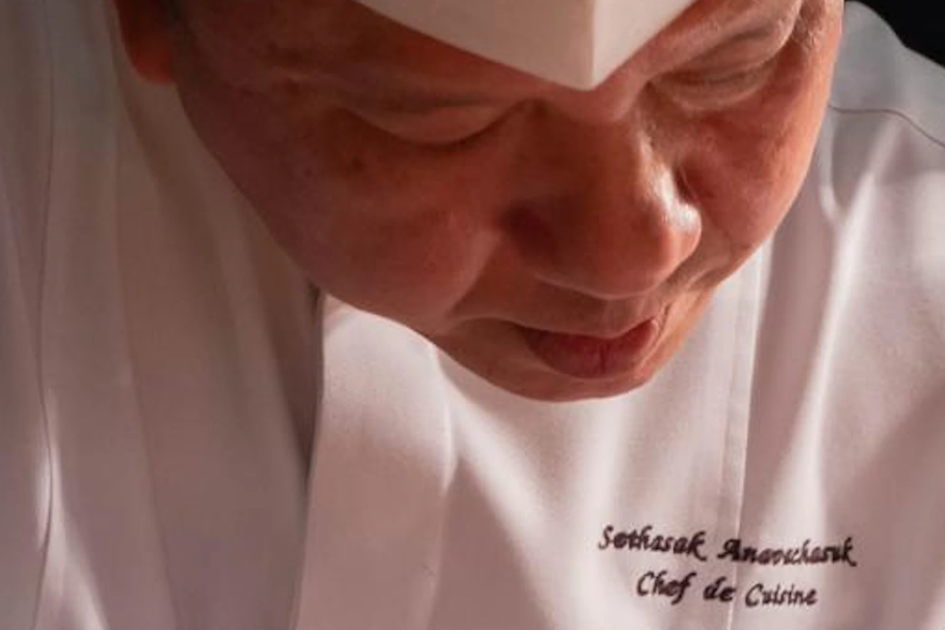 A chef in a white uniform slicing beef Wellington on a wooden cutting board, with dishes of food nearby.