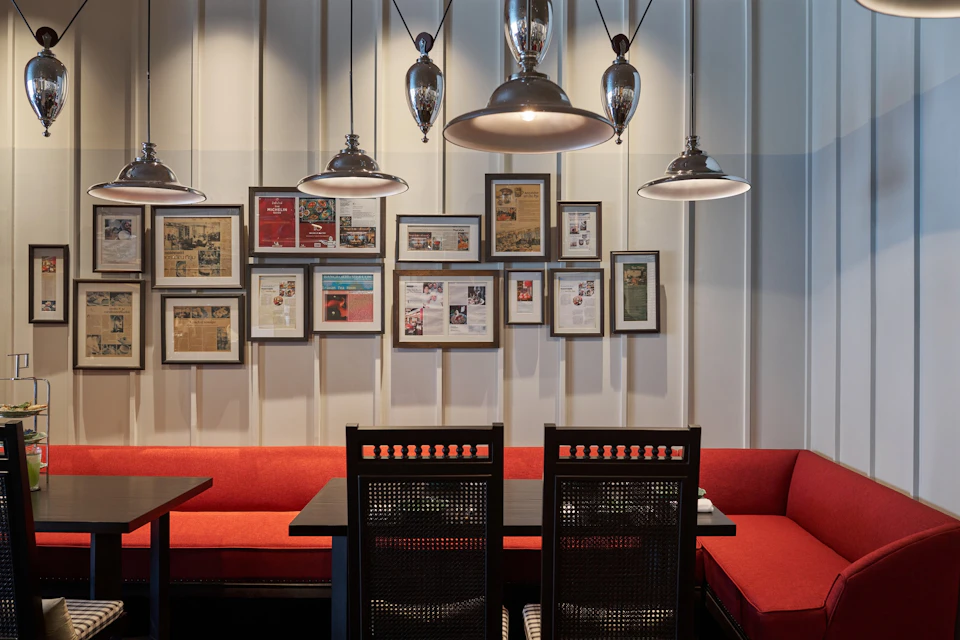 A restaurant interior with red cushioned seating, black chairs, framed pictures on the wall, and pendant lights overhead.