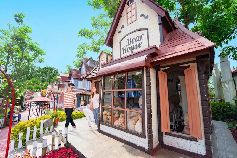 A family walks past a toy store labeled 'Bear House' with a variety of stuffed animals displayed in the window.