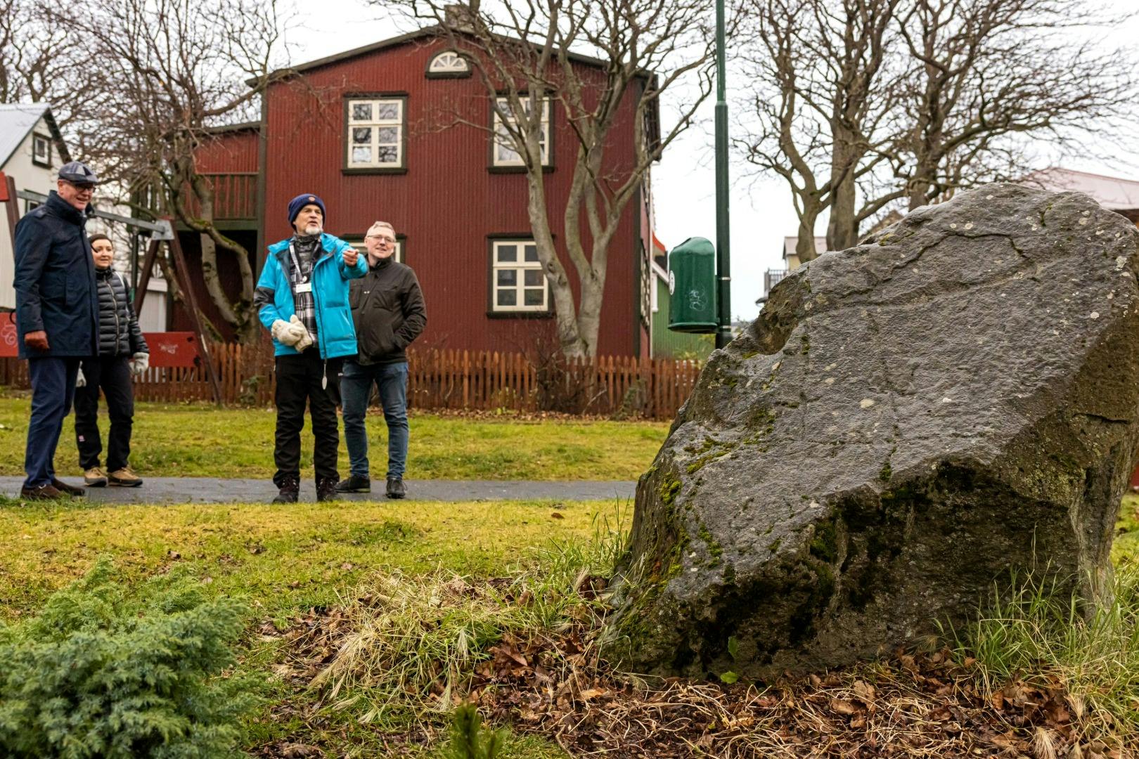 빨간색 주택과 나뭇잎이 없는 나무를 배경으로 길 근처의 풀밭에 네 사람이 서 있습니다.
