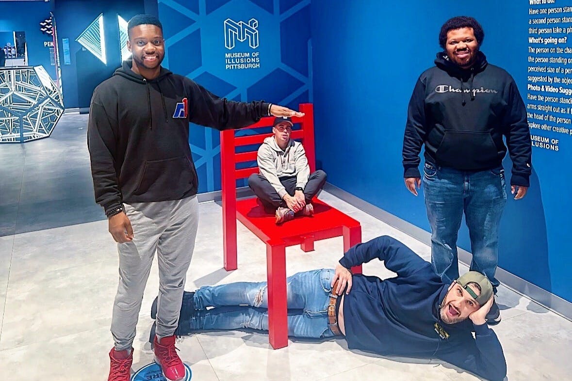 Vier mannen poseren in een gedwongen perspectief tentoonstelling met een gigantische rode stoel in het Museum of Illusions Pittsburgh.