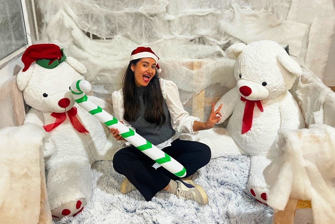 一位戴着圣诞老人帽子的女士坐在两只大毛绒北极熊之间，拿着条纹糖果拐杖道具，微笑着。