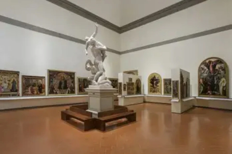 A museum gallery with a central marble statue on a pedestal, surrounded by paintings displayed on walls and partitions.