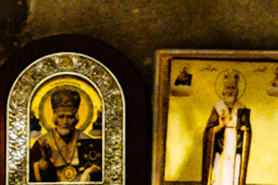 Hanging ornate lamps above icons of saints on a shelf, with an old paper bag on the left and a framed saint image on the right.