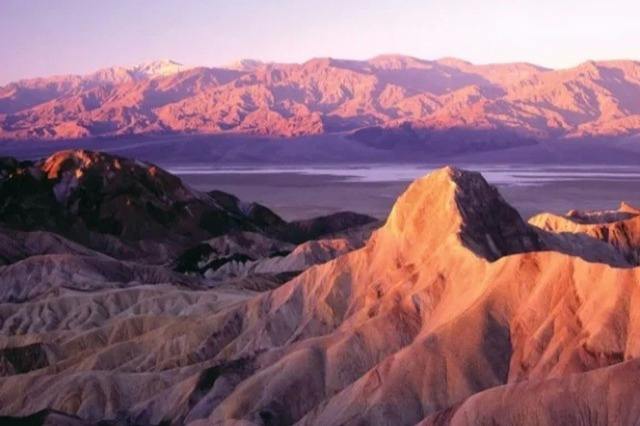 A scenic view of colorful desert mountains and rocky formations under a soft pink and purple sunset sky.