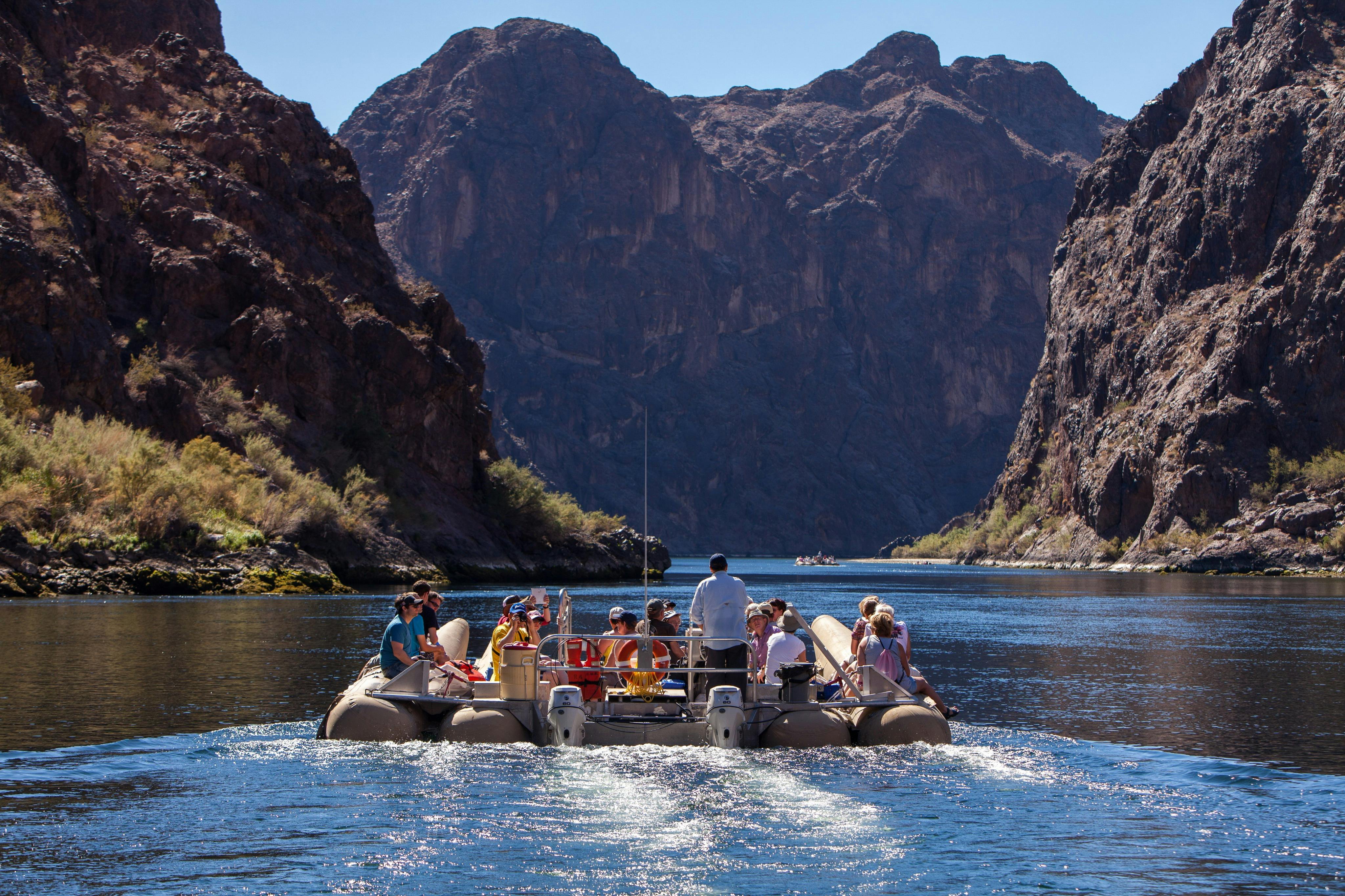 A group of people on a raft navigating through a river surrounded by rocky cliffs under a clear sky.