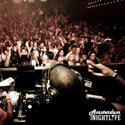 DJ som uppträder på en fullsatt nattklubb med folk som dansar och höjer sina händer under färgstark belysning. "Amsterdam Nightlife" -logotypen i hörnet.
