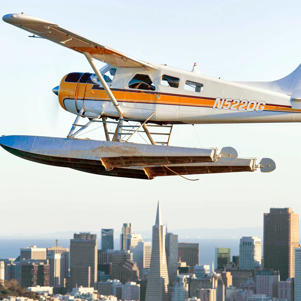 A seaplane with tail registration N5220G flying over a cityscape featuring a distinctive pyramid-shaped building.