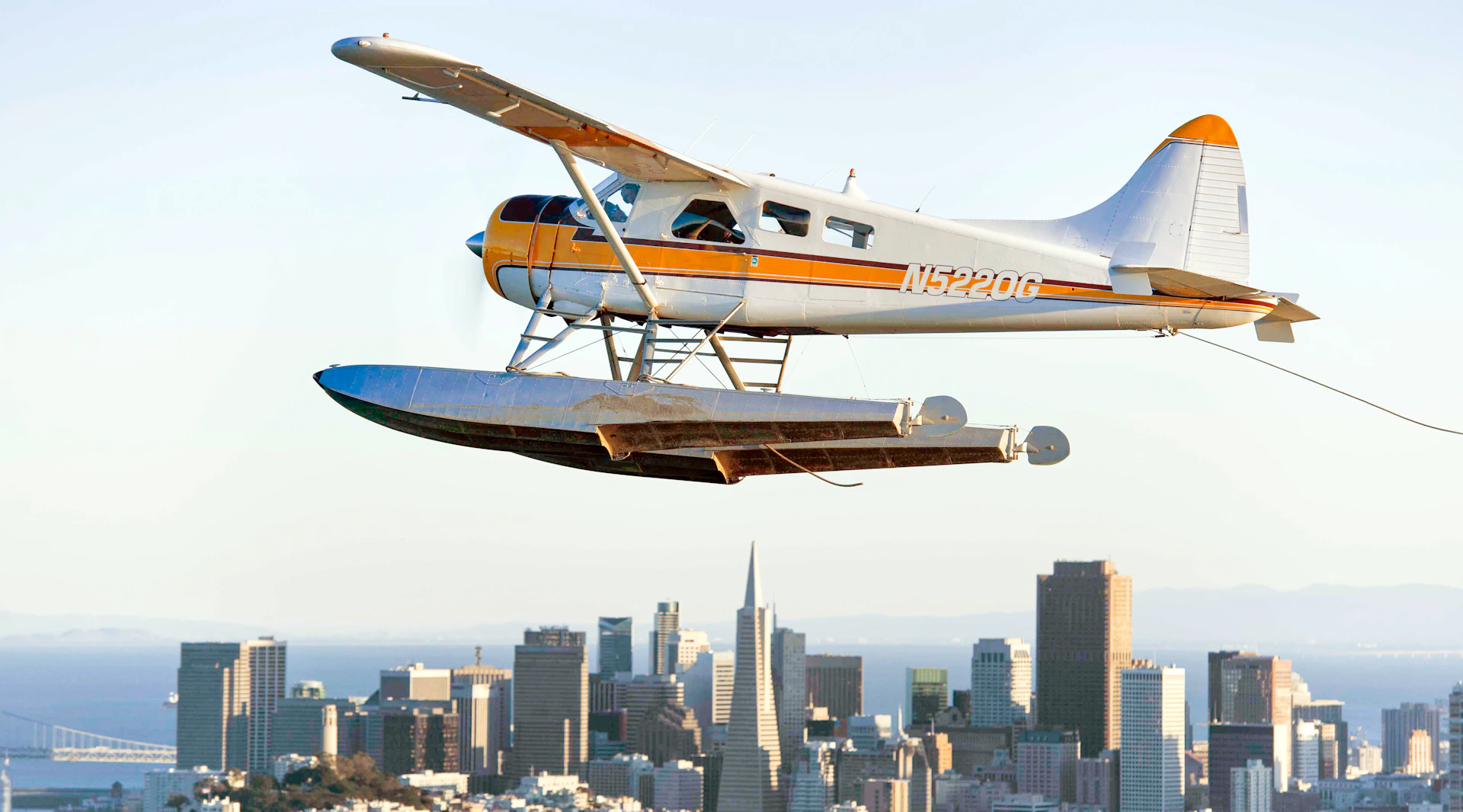 A seaplane with tail registration N5220G flying over a cityscape featuring a distinctive pyramid-shaped building.