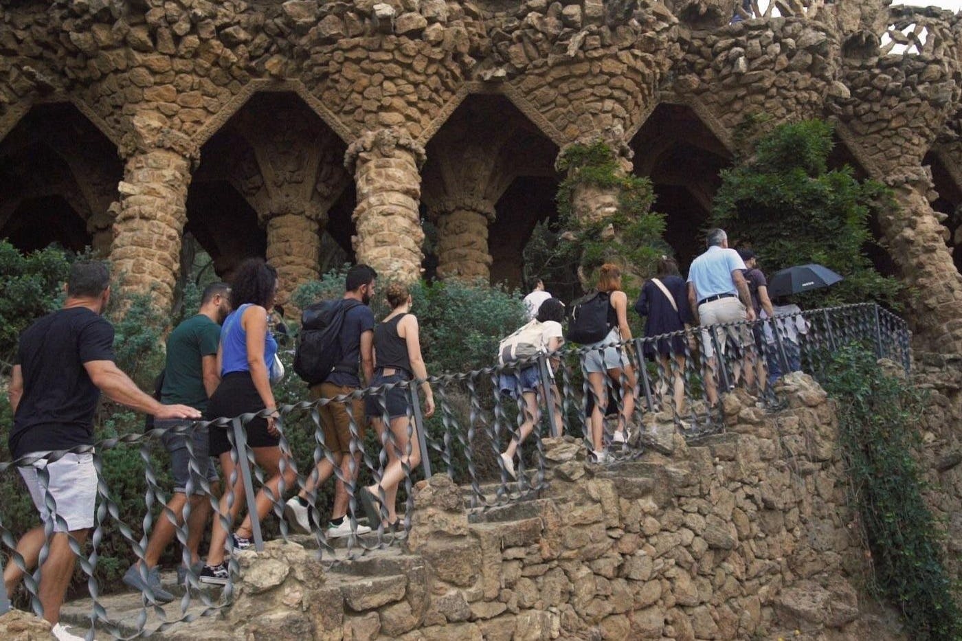 Un groupe de personnes montant un escalier en pierre près d'une structure en pierre ornée d'arches et de verdure.
