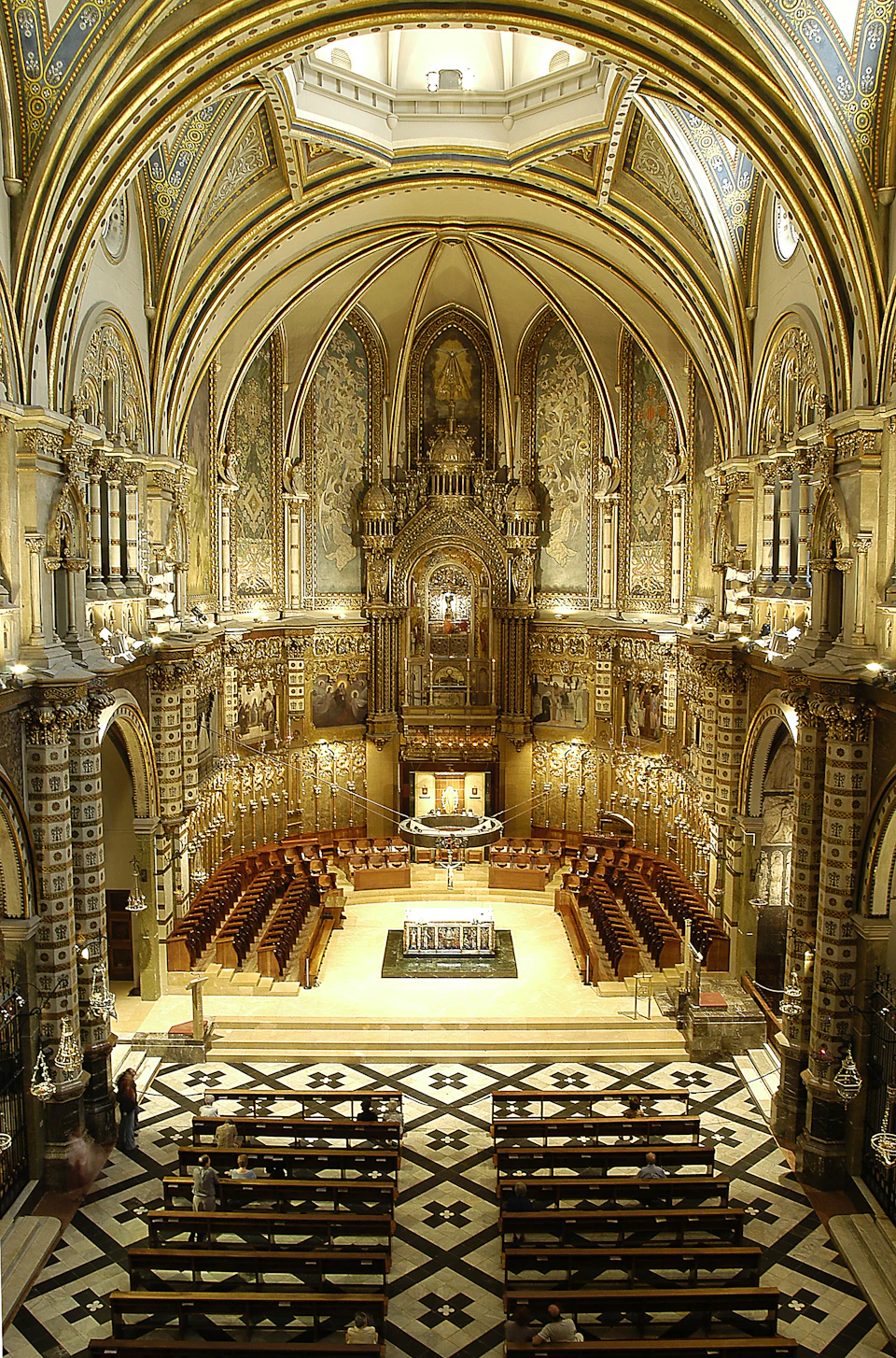 Grand, ornate cathedral interior with elaborate arches, gilded detailing, and symmetrical seating facing an ornate altar.