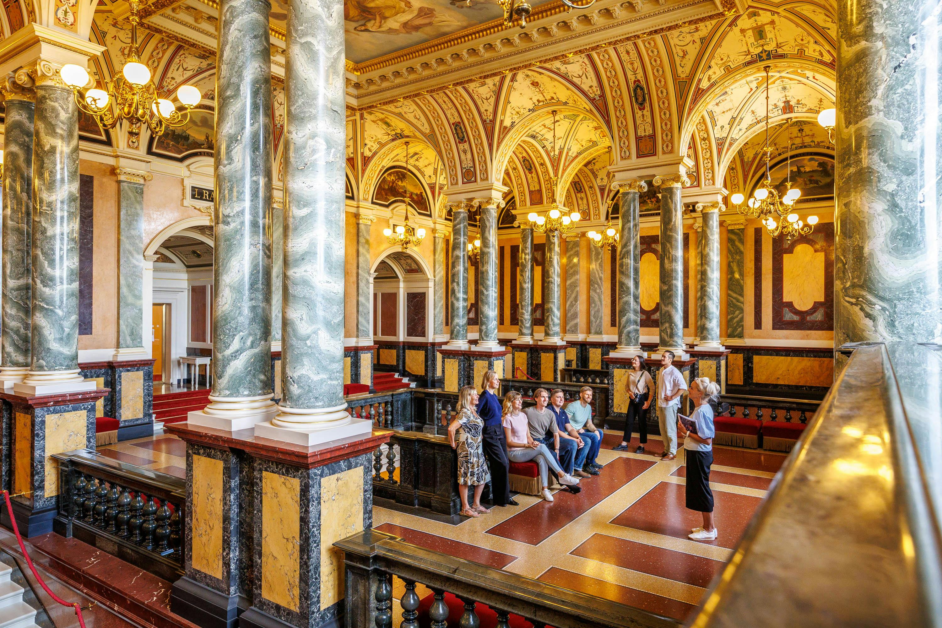 A group of people in a grand interior with ornate columns, arched ceilings, and decorative lighting.