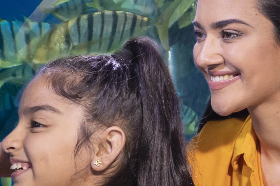 A woman and a young girl in yellow outfits admire fish and stingrays through an aquarium glass.